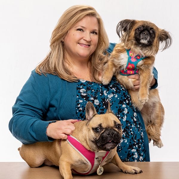 Hospital Director, Kim Ward, smiling happily and holding her two brown pet dogs, one smooth and one fully