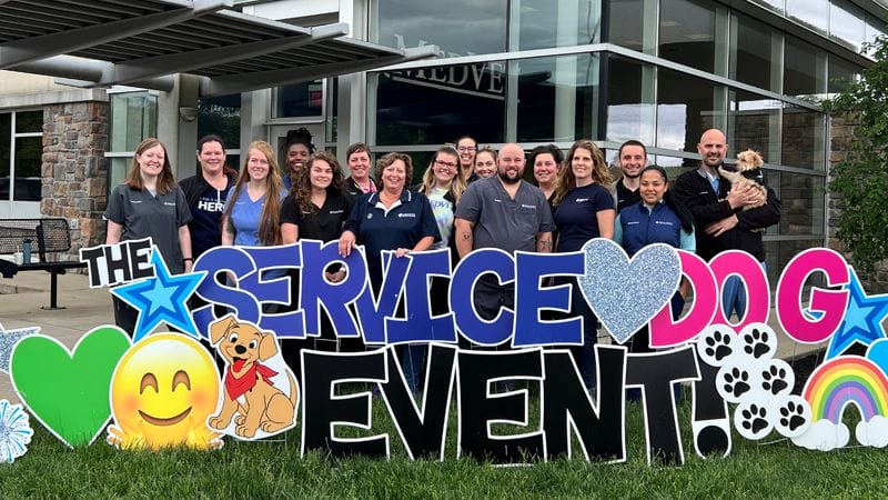 MedVet Cincinnati team members standing behind large yard sign that says, “The Service Dog Event!” out in front of veterinary hospital